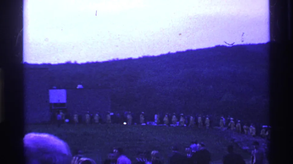 A wide 1969 Ohio home-movie view shows the formation extending across the field, with spectators or nearby viewers partly visible in the foreground.