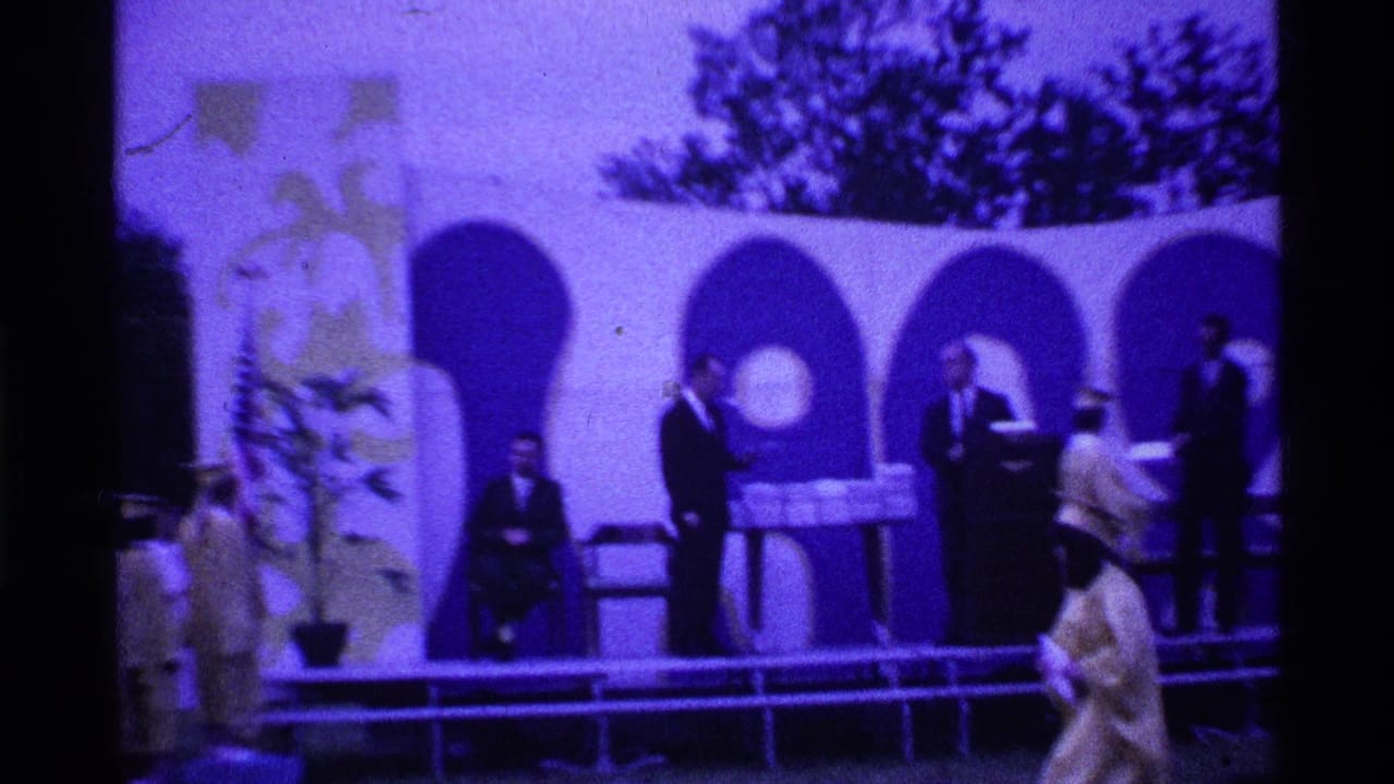 1969 Ohio graduation footage showing a graduate crossing an outdoor stage toward suited officials near a diploma table and arched backdrop.