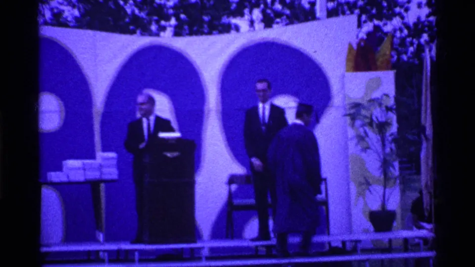 The 1969 Ohio commencement scene shows a graduate facing officials on the stage, with arched panels, a podium, chair, and potted plant visible.