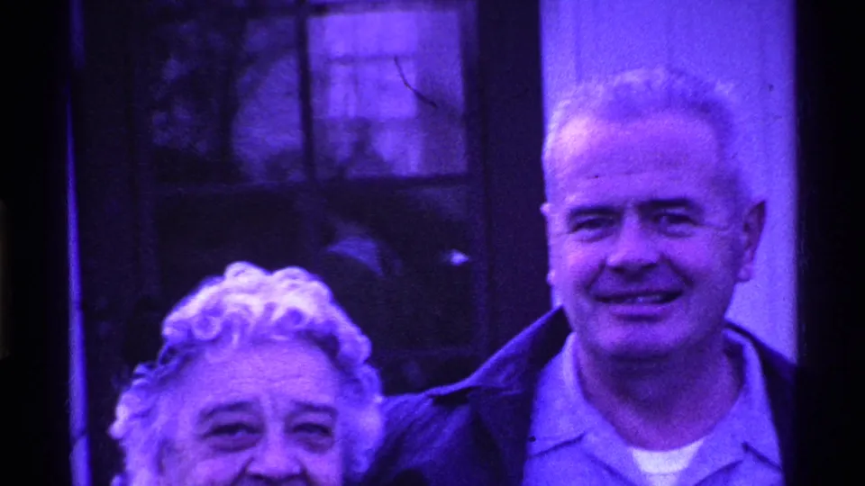 The 1969 Ohio home-movie frame shows the older couple in a tight crop, smiling near a window and exterior wall.