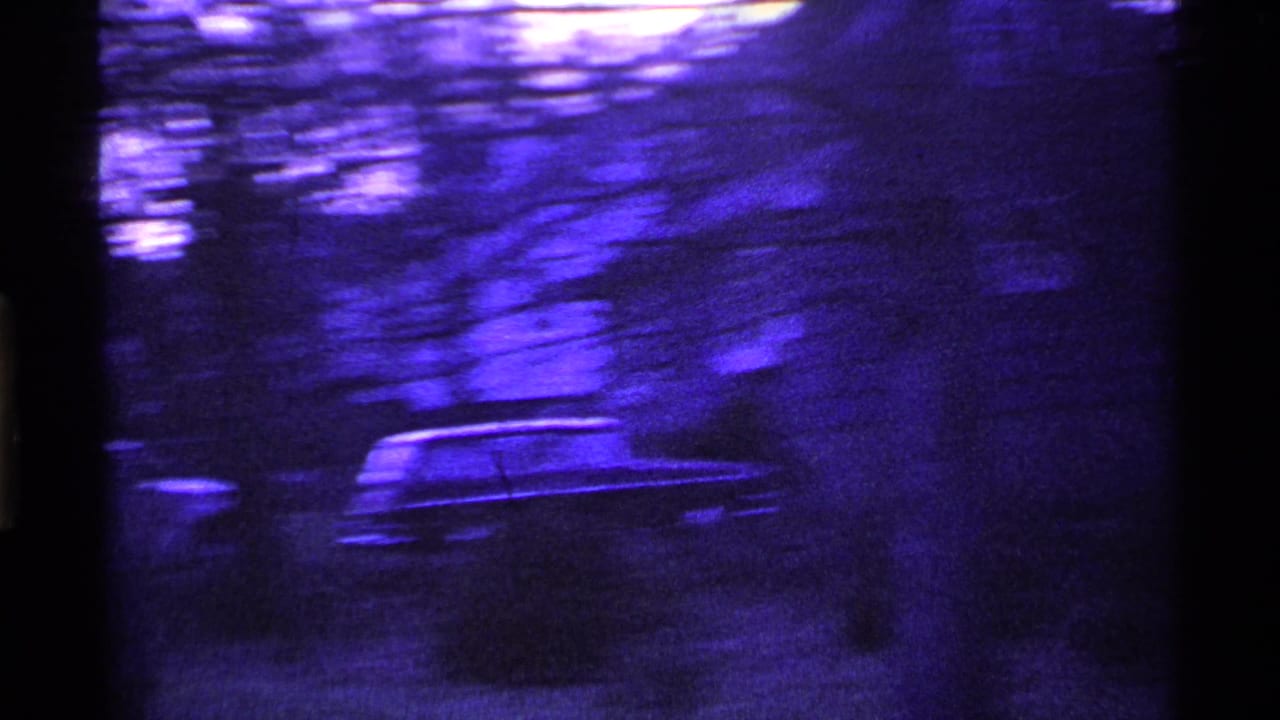 1969 Ohio 8mm frame showing a blurred parked car beyond bare trees, with heavy grain and a purple color cast.