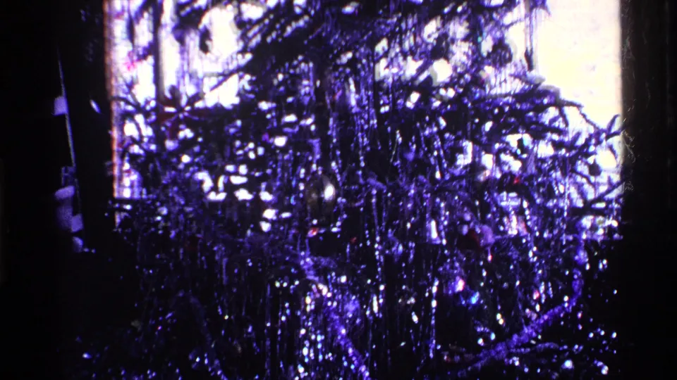 1969 Ohio 8mm frame showing a tinsel-covered Christmas tree in a dim private room with strong purple color cast.