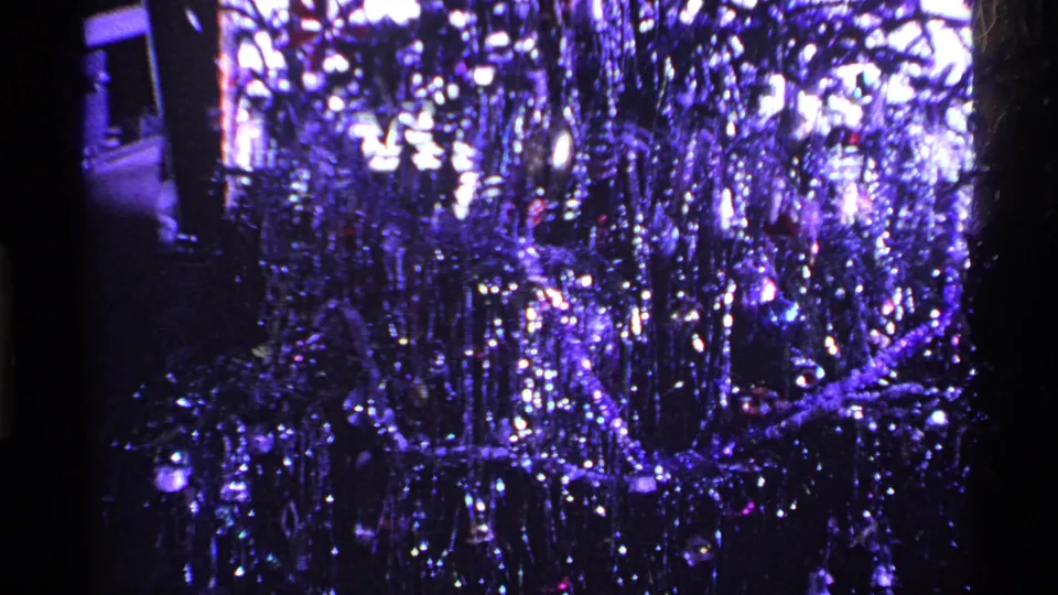 1969 Ohio home-movie frame of a decorated Christmas tree with reflective tinsel and ornaments in a dim interior.