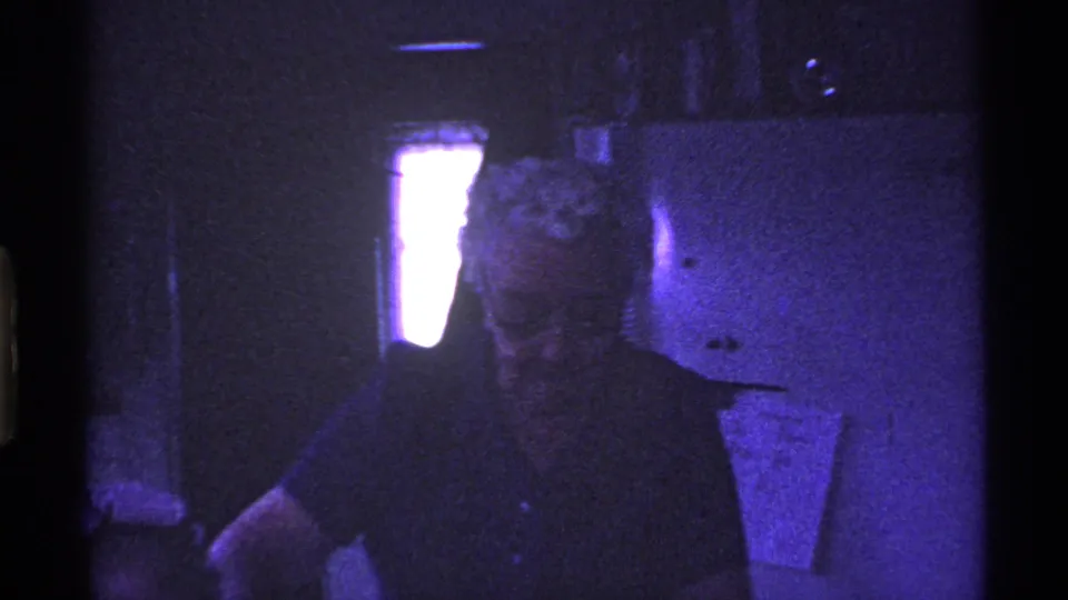 1969 Ohio 8mm frame showing an older woman in a dark top near kitchen cabinets inside a private home.