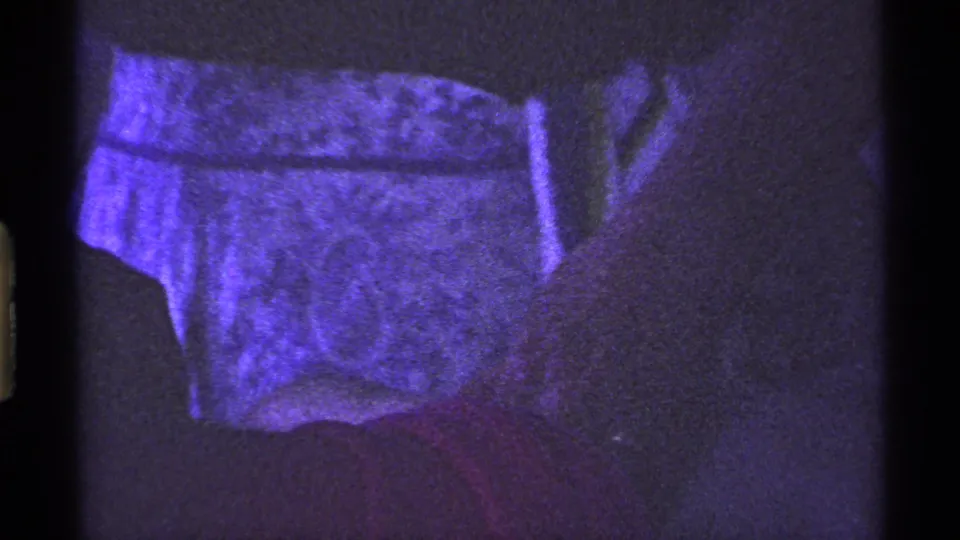 1969 Ohio 8mm frame with patterned clothing and red fabric visible in a dim private interior with pronounced grain.