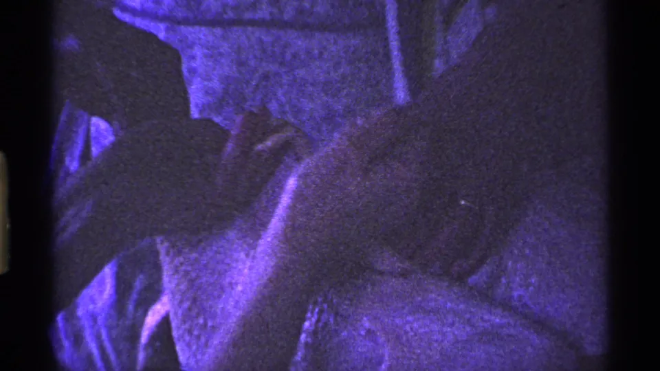 Final 1969 Ohio 8mm frame showing a child or young person leaning near bedding or upholstery in a purple-lit private room.