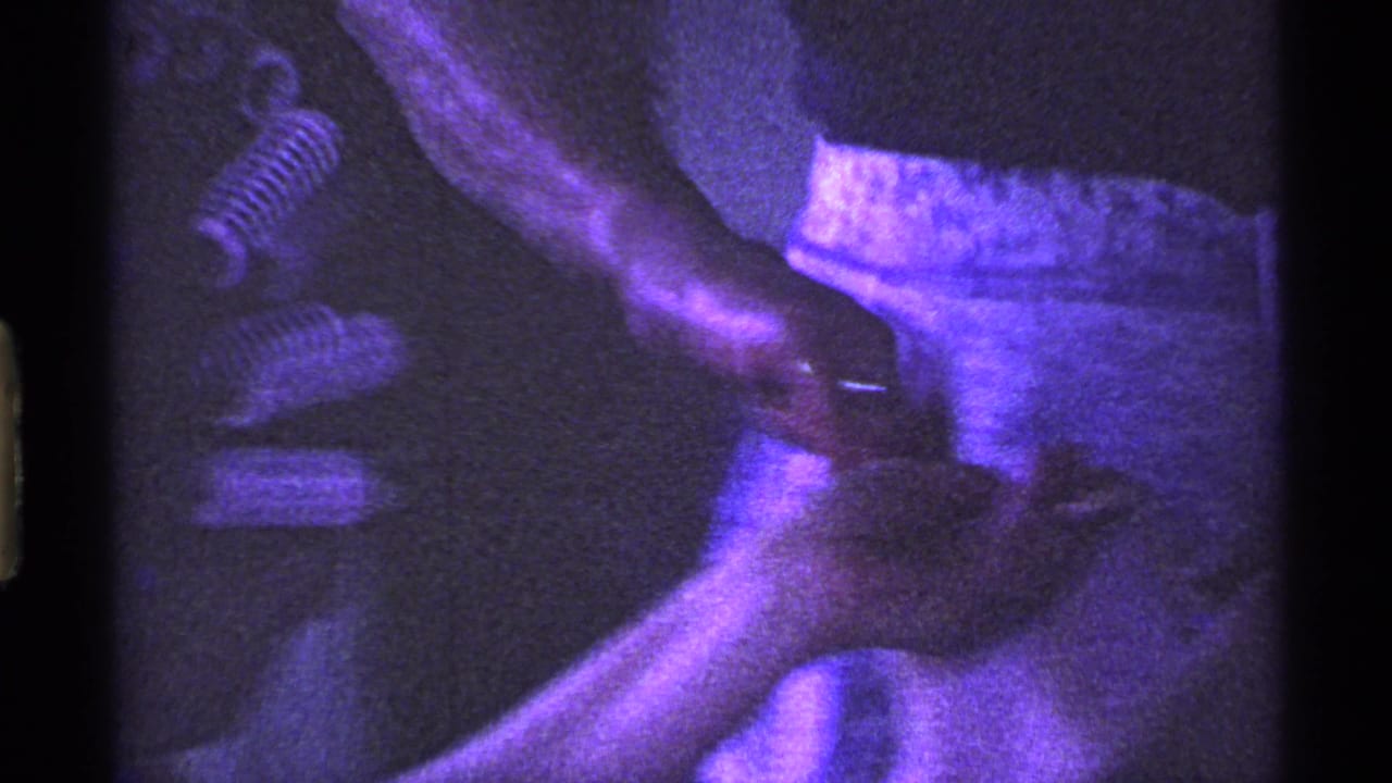 In this 1969 Ohio home-movie frame, hands work inside a turkey on a kitchen surface beside a light apron and dark shirt.