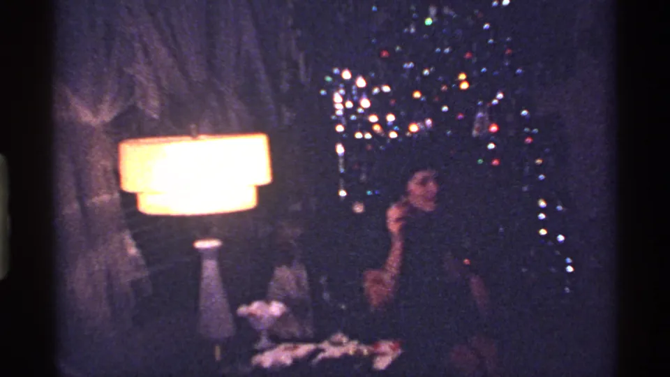 1969 Ohio holiday frame showing a woman in a dark dress seated beside a decorated Christmas tree and lamp.