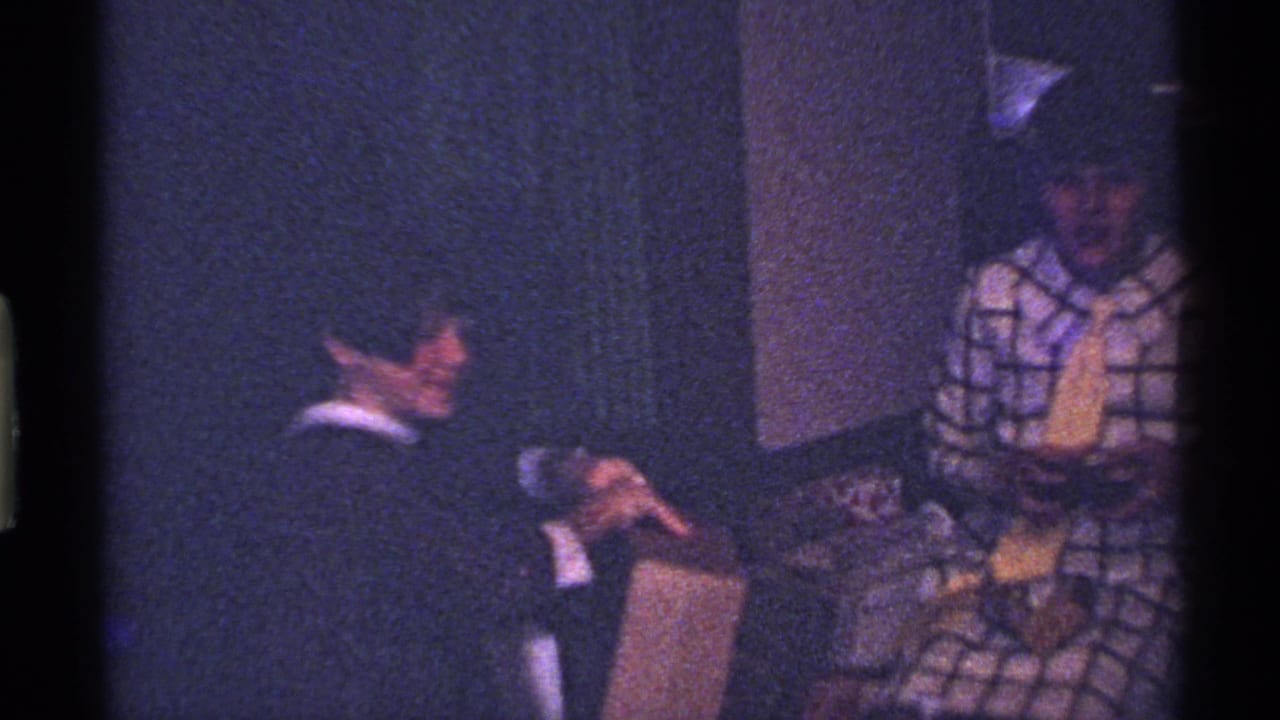 Child in a dark suit holds a gift box while another child in plaid stands nearby.