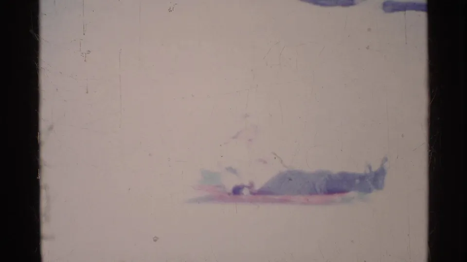 1969 Ohio home-movie frame with a bundled person stretched out on a sled in bright snow.