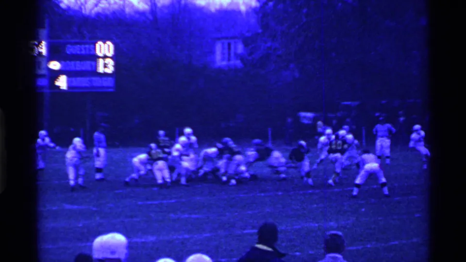 1969 Ohio high school football players line up at night, with a scoreboard and sideline spectators in a blue-tinted 8mm frame.