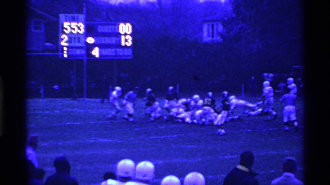 Ohio high school football players converge near the line of scrimmage during a 1969 night game, with the scoreboard behind them.