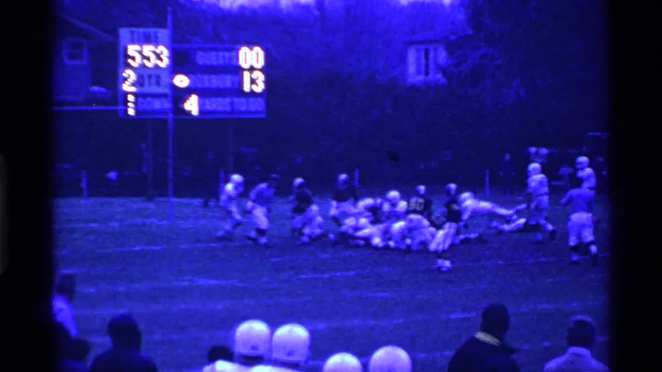 Ohio high school football players converge near the line of scrimmage during a 1969 night game, with the scoreboard behind them.
