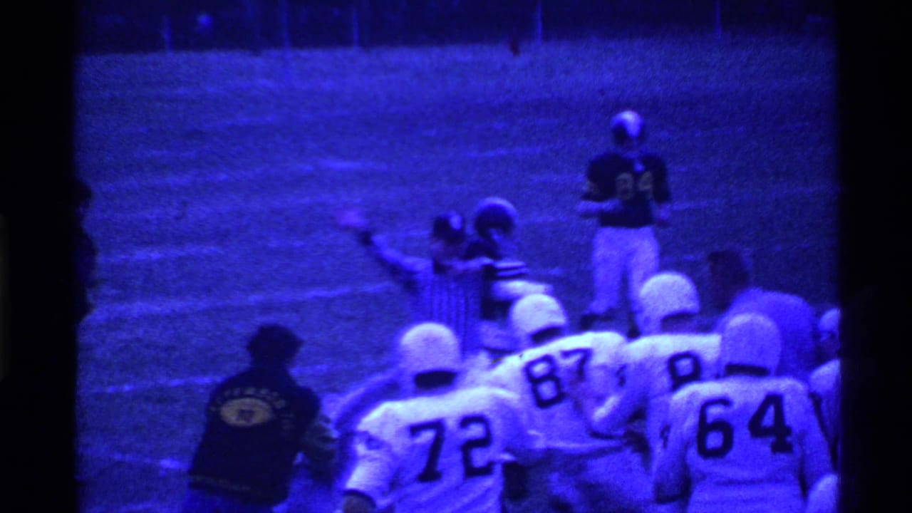A referee signals near football players lined along the sideline.