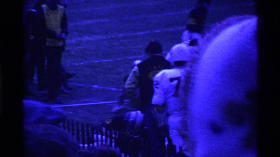 1969 Ohio home-movie footage shows football players near the sideline with a foreground spectator partly blocking the view.