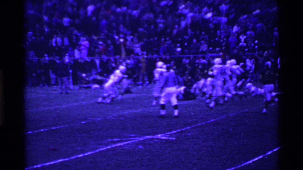 1969 Ohio football game footage with players in motion under purple-tinted 8mm stadium lighting.