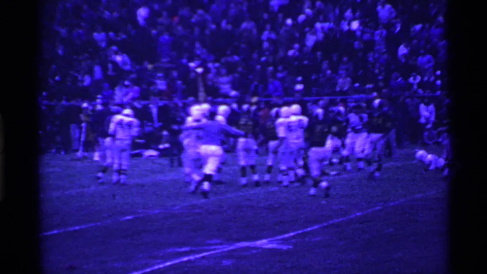 Home-movie view of a 1969 Ohio high school football game, with players clustered near the sideline and bleachers behind them.