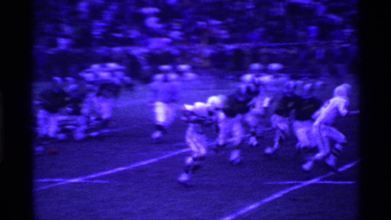 1969 Ohio home-movie frame showing a football play beginning near the line, with players clustered under blue-purple film tint.