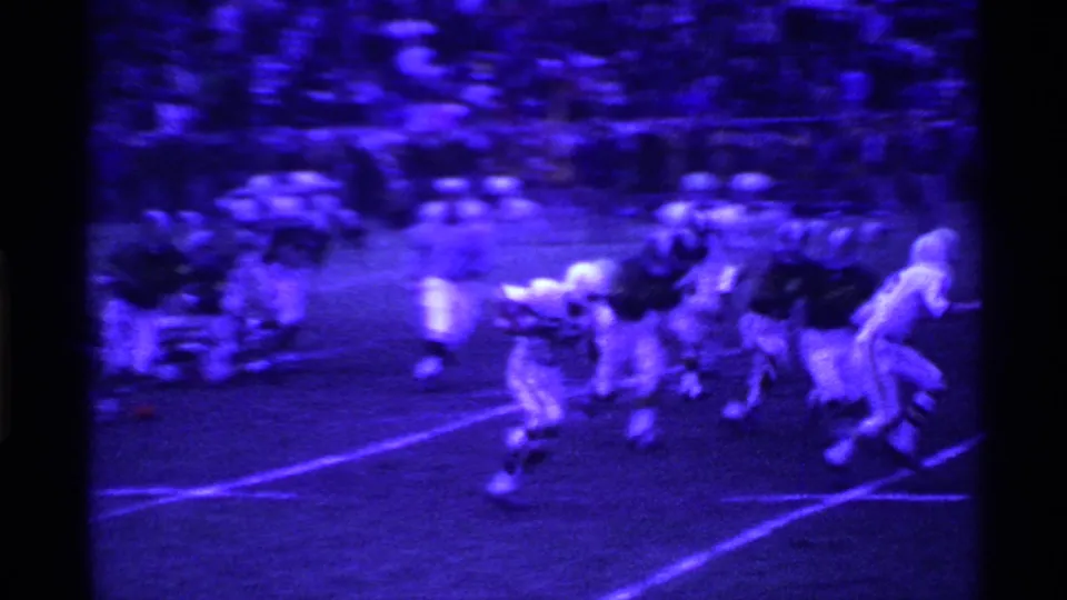 1969 Ohio home-movie frame showing a football play beginning near the line, with players clustered under blue-purple film tint.