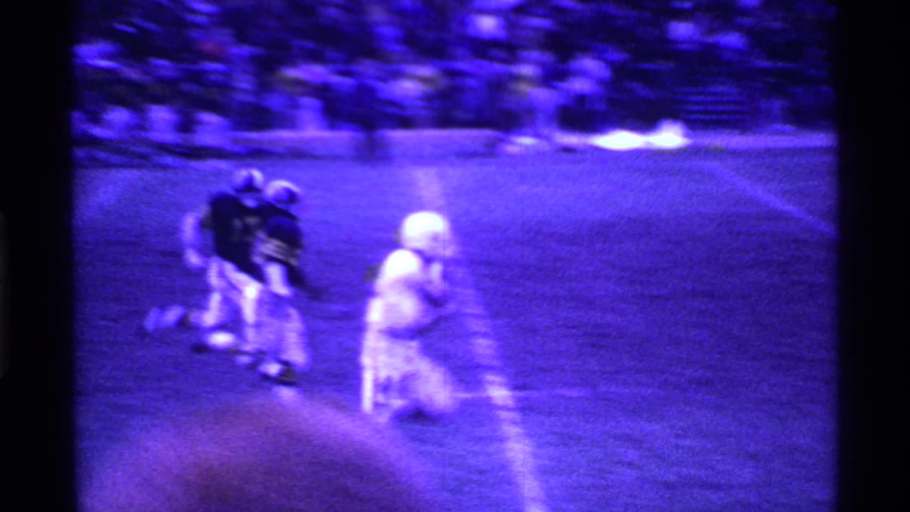 A white-uniformed runner carries the football down the sideline as defenders trail behind.
