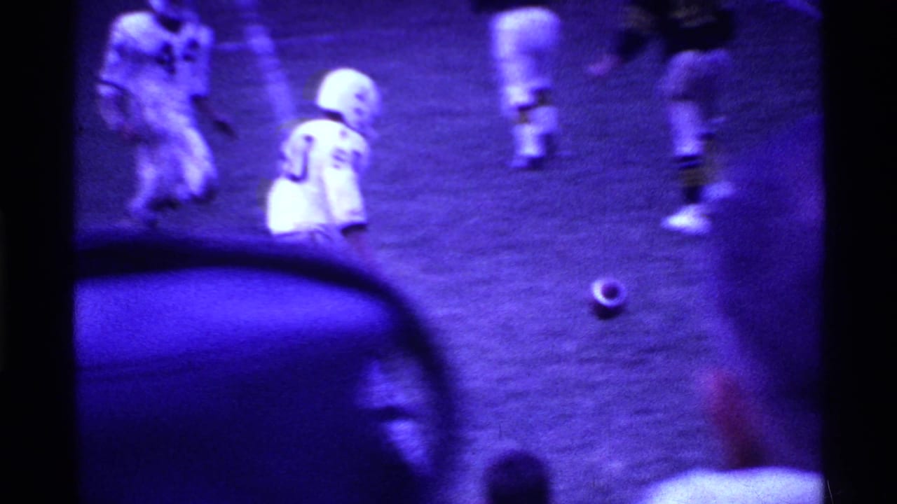 Football players stand and move near a football on the grass field.