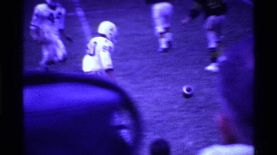 Purple-tinted 8mm frame of a 1969 Ohio football play with players in white uniforms near the ball on the field.
