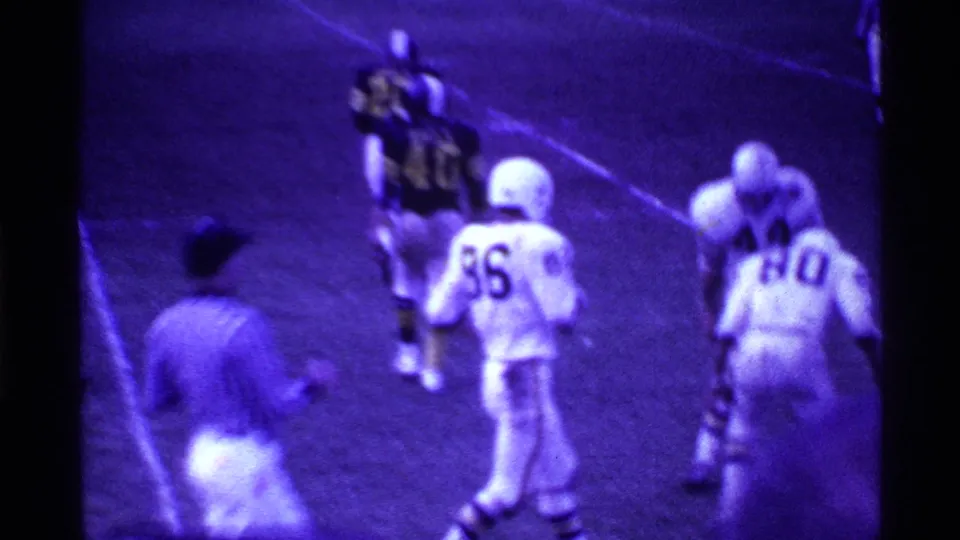 1969 Ohio football footage frame showing a dark-uniformed player near white-jerseyed opponents and a sideline figure.
