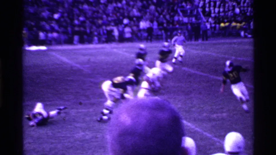 Sideline home-movie view of a 1969 Ohio football play, with players in motion and a spectator head partly obscuring the lower frame.