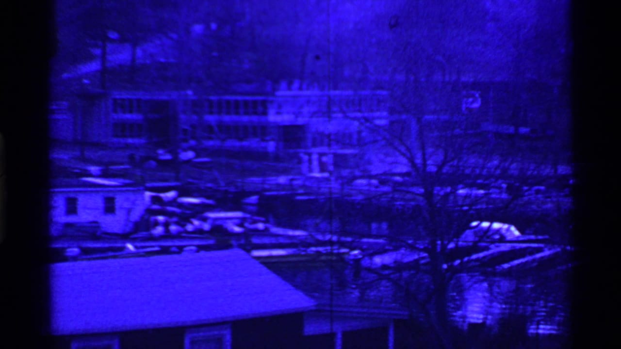 Blue-toned lakeside houses, docks, bare trees, and boats viewed across water.
