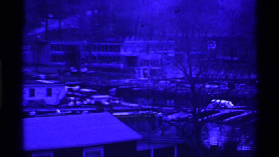 Ohio 1969 8mm frame showing a blue monochrome lakeside community with houses, docks, bare trees, and small boats near the shore.
