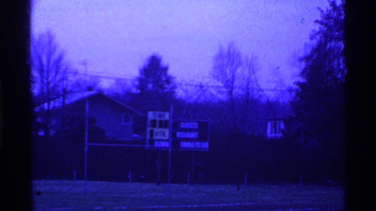 Empty field with scoreboard and trees, split by dark film-frame borders.