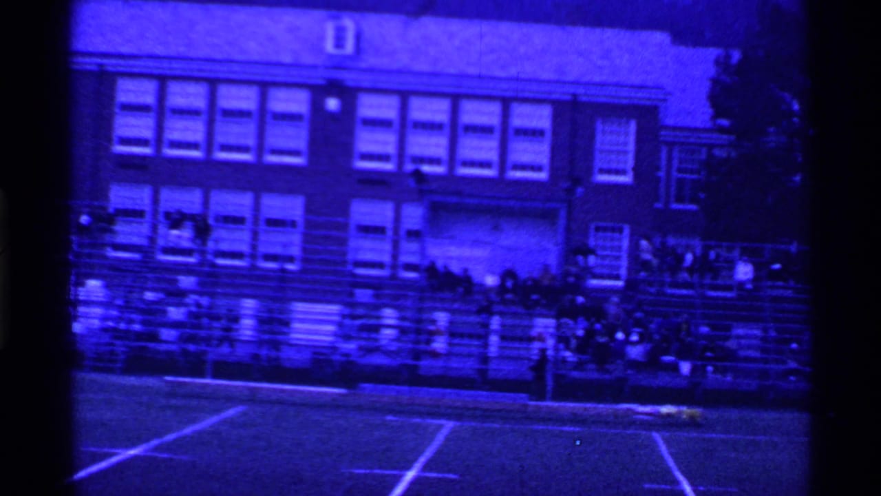 Bleachers with scattered spectators in front of a brick school building.