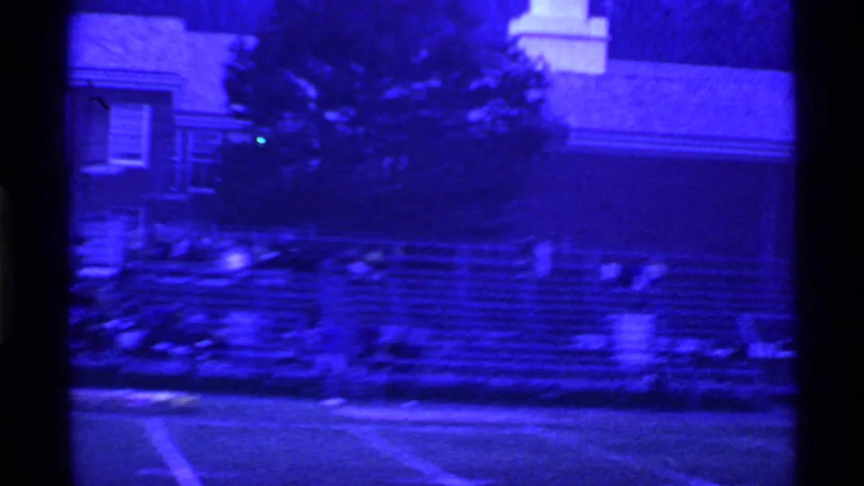 Blue-tinted 8mm view of an Ohio school athletic area, with blurred bleachers, field lines, and part of the building visible.