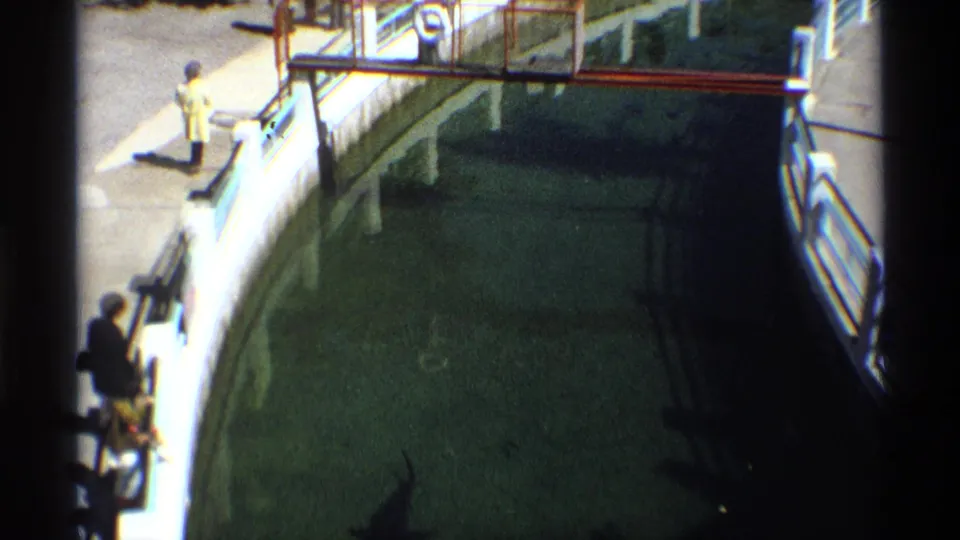 Curved public aquarium walkway with visitors looking down into the green tank water, filmed on 8mm.