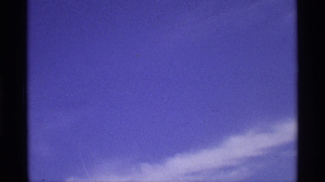 Metadata-supported 1970 8mm home-movie frame showing blue sky, wispy white cloud, dark scan borders, and a faint purplish film cast.