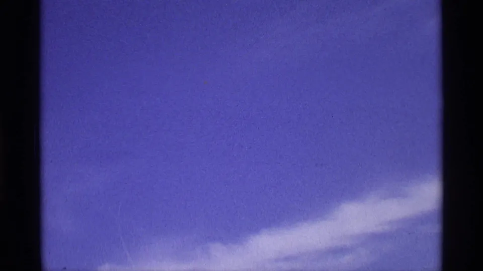 Metadata-supported 1970 8mm home-movie frame showing blue sky, wispy white cloud, dark scan borders, and a faint purplish film cast.