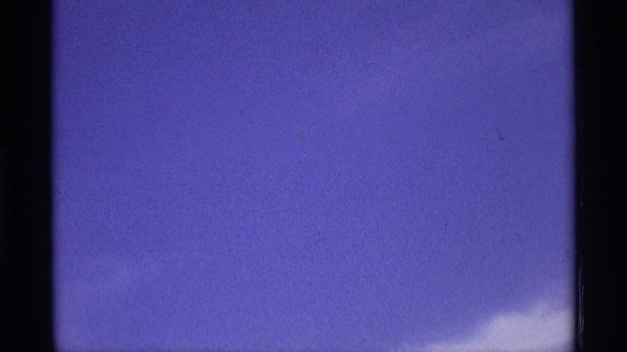 Mostly blue sky with a small wispy cloud near the lower right and dark film edges.