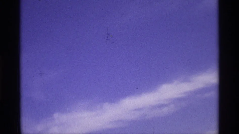 Metadata-supported 1970 8mm home-movie frame showing a broad pale cloud band near the lower left, blue sky, dark film borders, and visible grain.