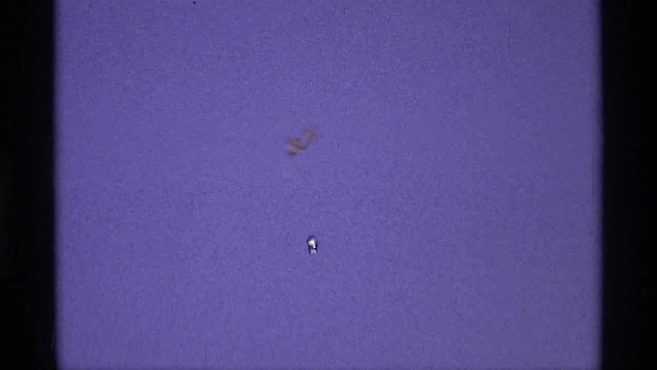 Purple-tinted 8mm film frame with gate edges, dust, and small marks.