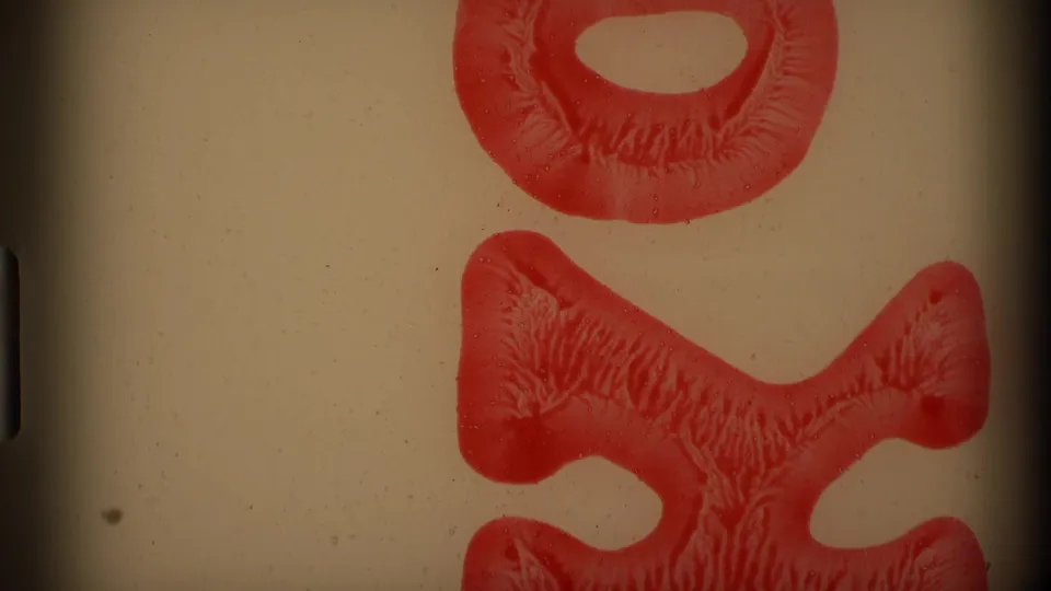 Beige-tinted 8mm frame with a large red vertical abrasion or exposed film shape and visible grain.