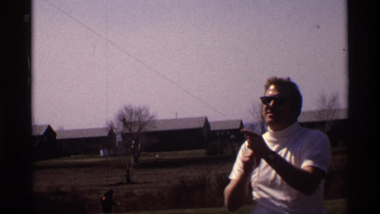 Man in sunglasses and a white shirt holds kite string in a grassy field.