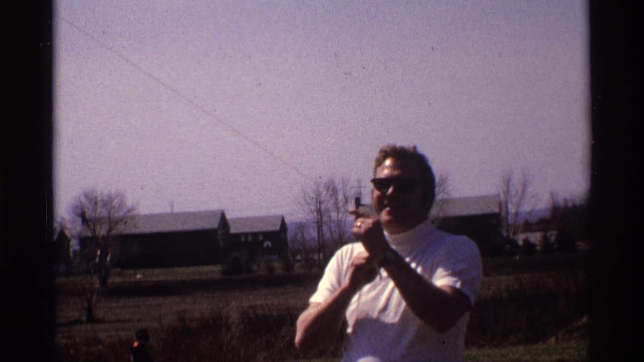 Man in dark sunglasses adjusts kite string against a pale sky and rural backdrop.
