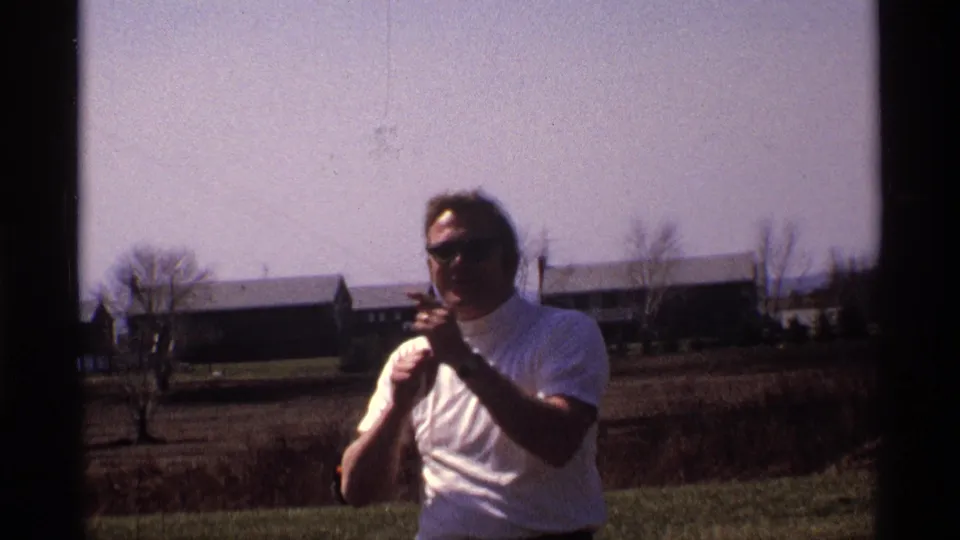 A 1970 home-movie view in Florida, Michigan frames the man with sunglasses and kite string below a broad pale sky.