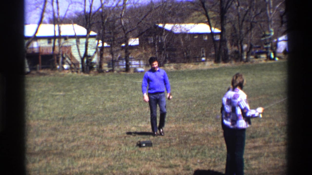 Man walks closer while a person at right holds a kite line in the yard.