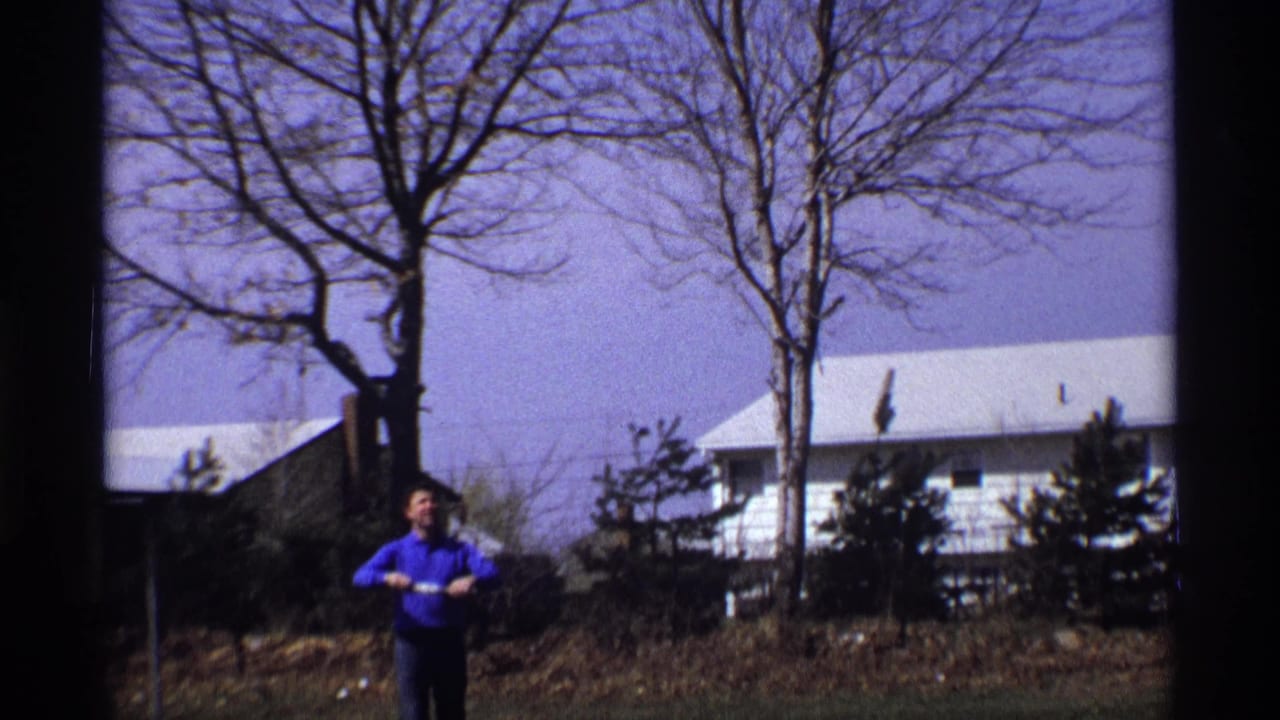 Man in a blue shirt stands in a backyard beneath bare trees and a pale sky.