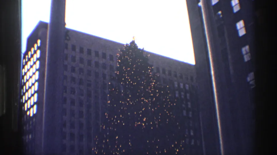 Low-angle 1970 New York City holiday frame with the Rockefeller Center tree lit against office windows.