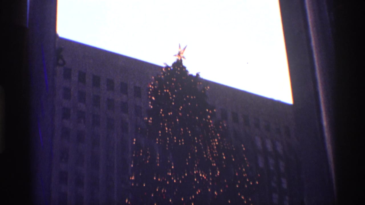 Rockefeller Center Christmas tree with small lights and a star topper against a dark building facade.