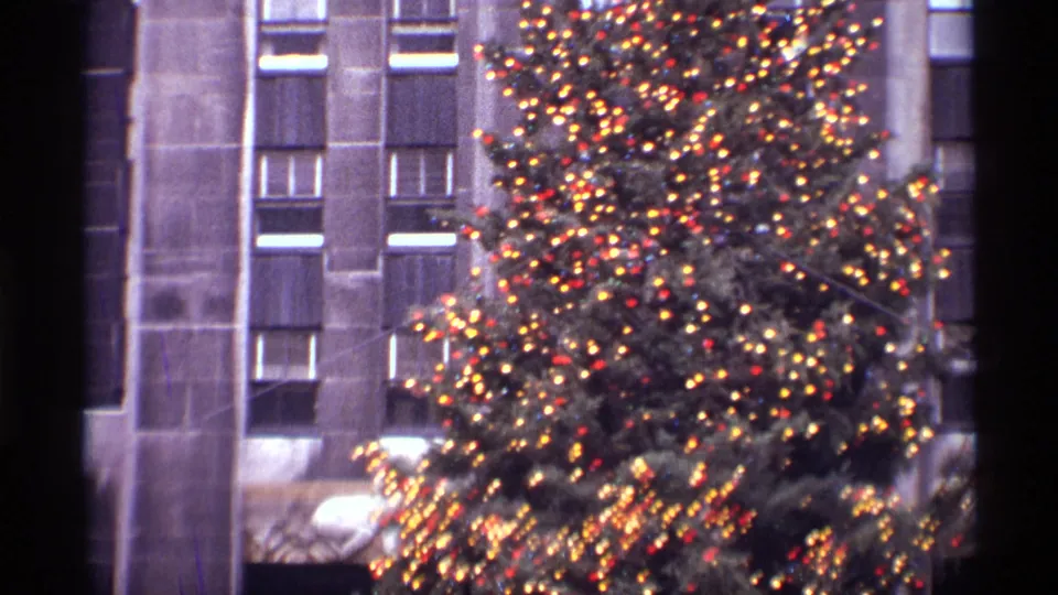 Final 1970 New York City frame showing the illuminated Rockefeller Center Christmas tree beside vertical stone architecture.
