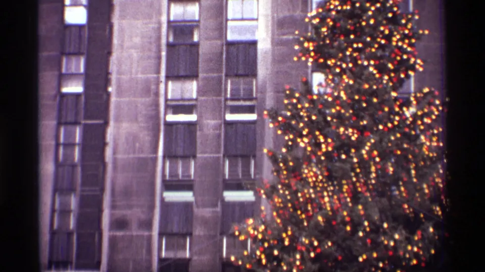 1970 New York frame with dense Christmas tree lights glowing beside the vertical facade of a Rockefeller Center building.
