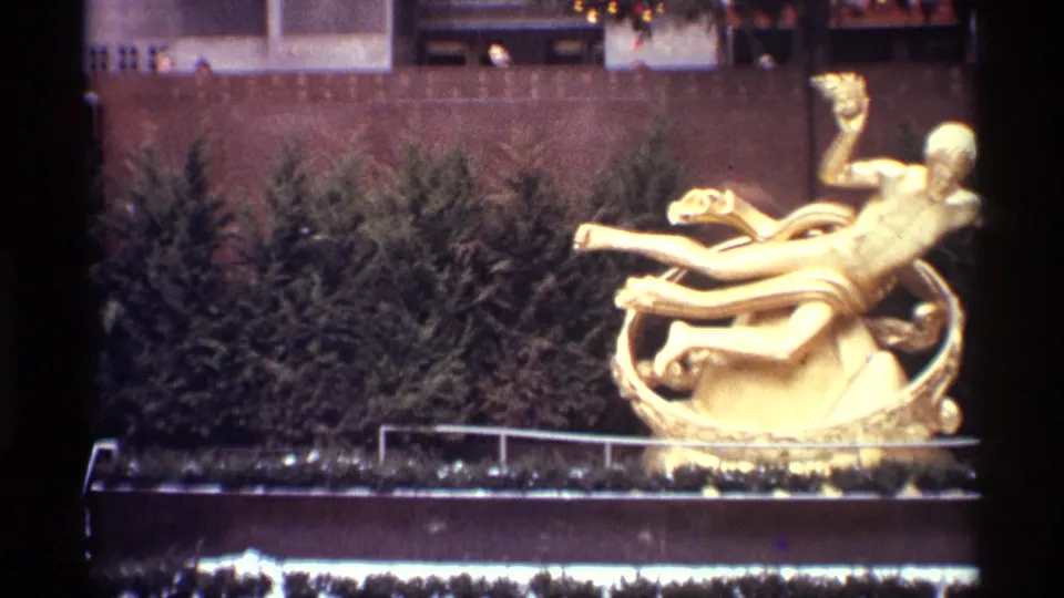 1970 New York City home-movie frame showing Prometheus in the lower plaza with the Christmas tree lights above.